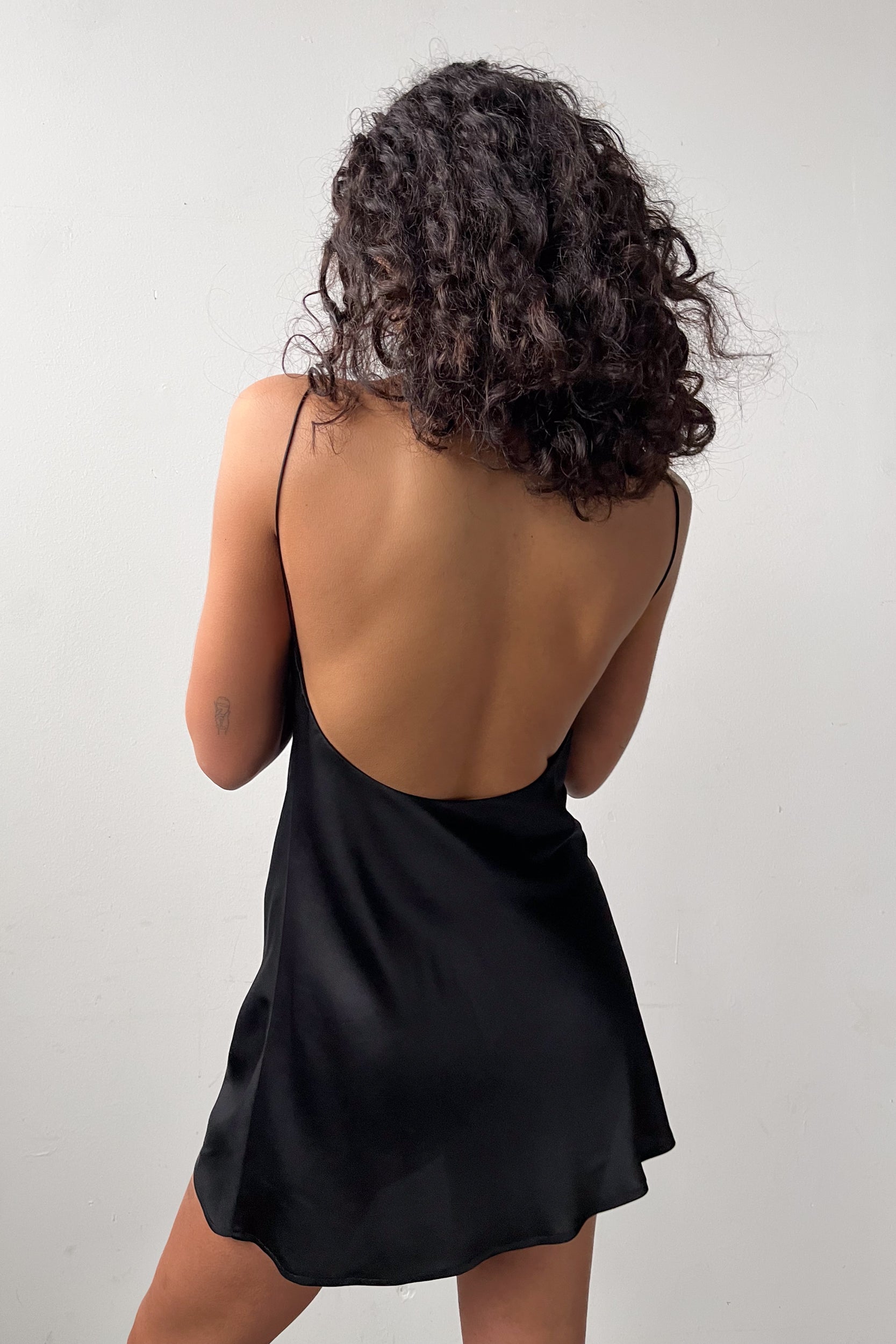 Rear view of the Backless Short Slip Dress in Black, featuring a flowing satin fabric and a flattering backless design.