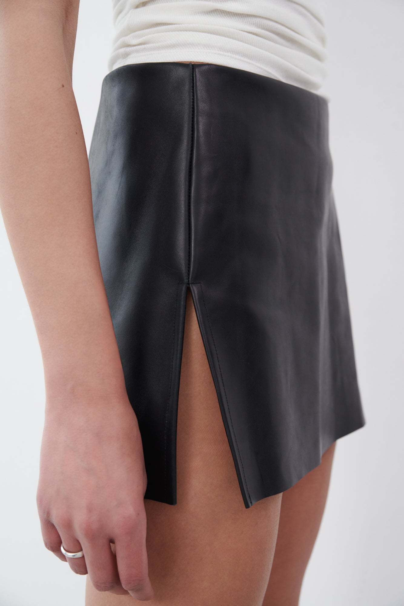 Close-up of black leather mini skirt with side slit detail, crafted from eco-friendly deadstock leather for an elongated silhouette.