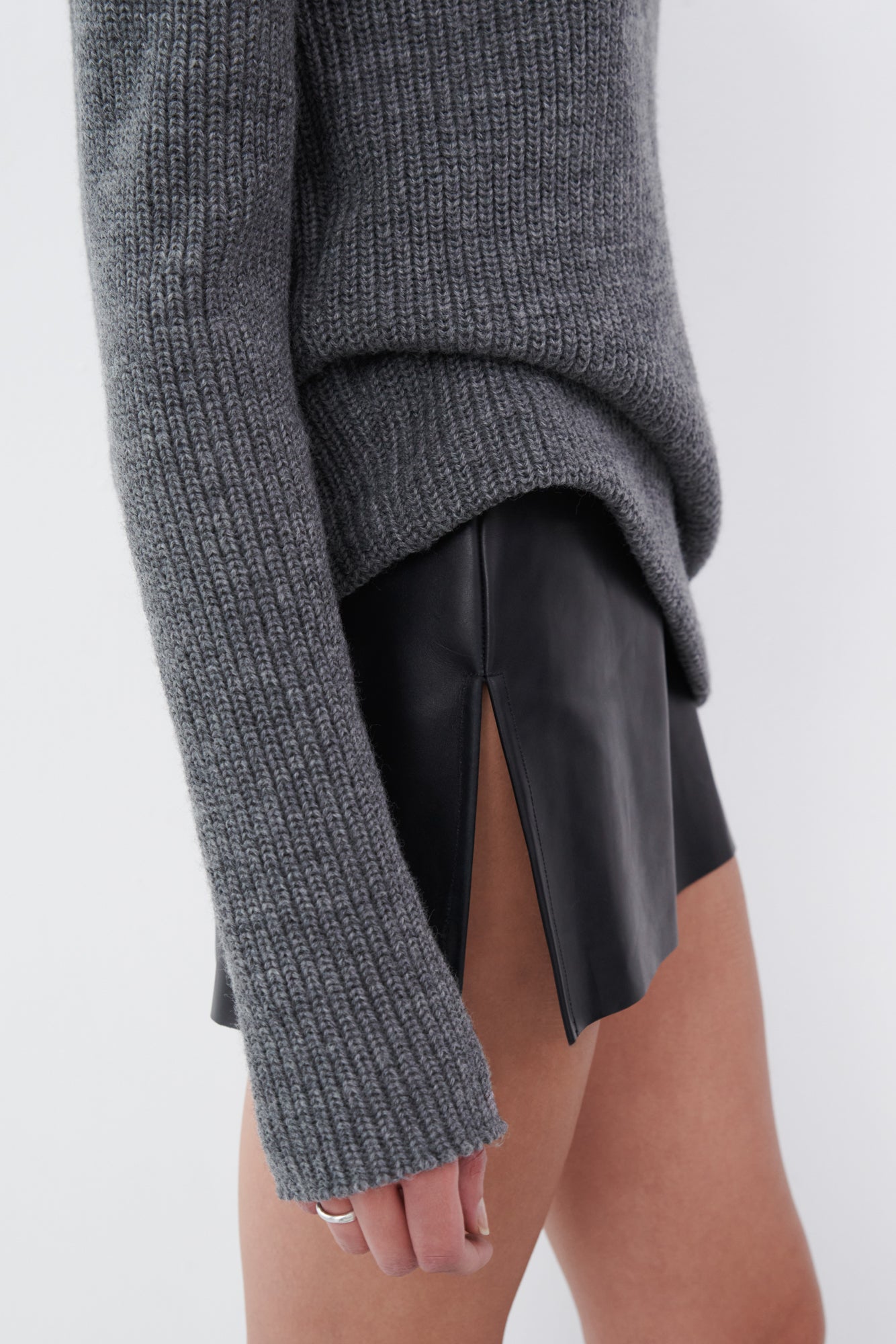 Black leather mini skirt with side slit detail paired with a gray knit sweater, blending edgy and cozy styles effortlessly.