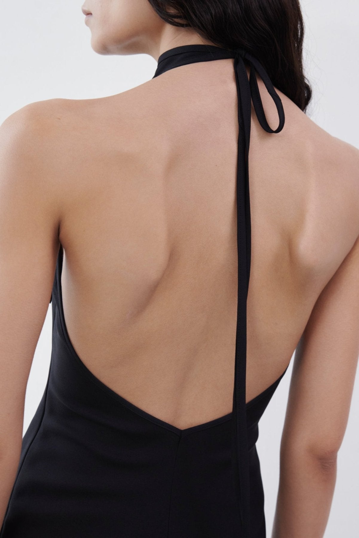 Close-up back view of a black backless halter maxi dress highlighting the open-back design and tie detail at the neck.