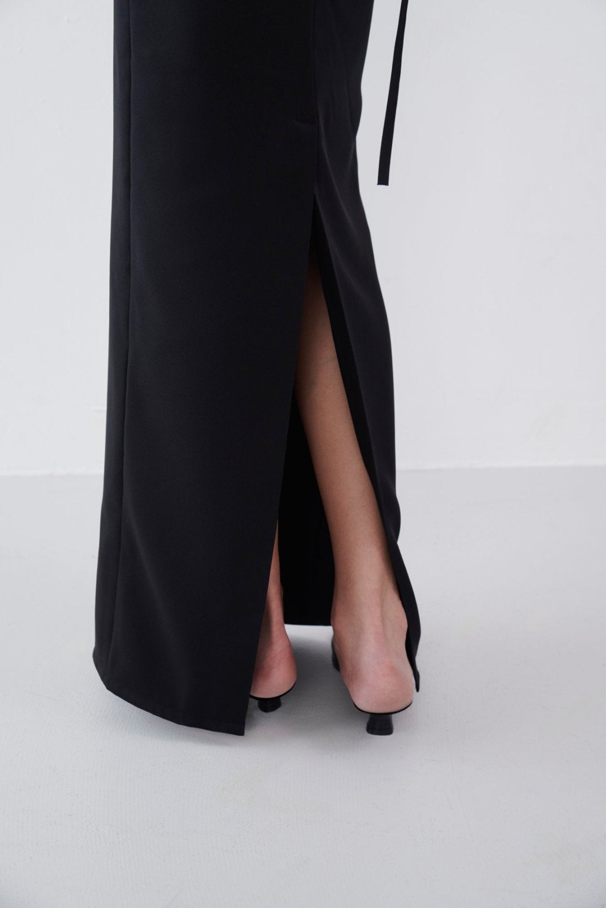 Close-up of the slit detail on a black maxi dress, revealing the lower leg and styled with black open-back heels.