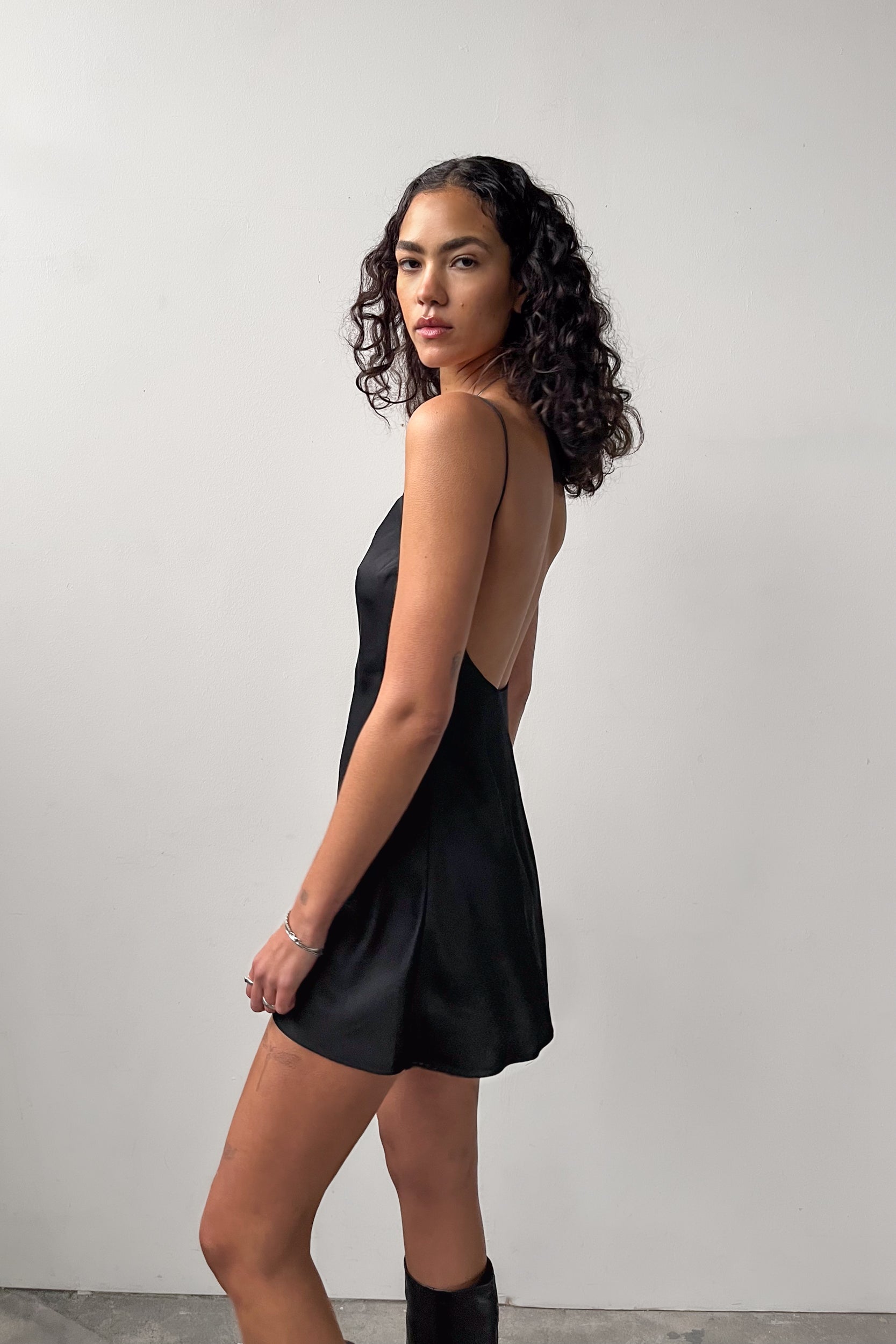 Side profile of the Backless Short Slip Dress in black, highlighting its soft satin material and elegant drape.