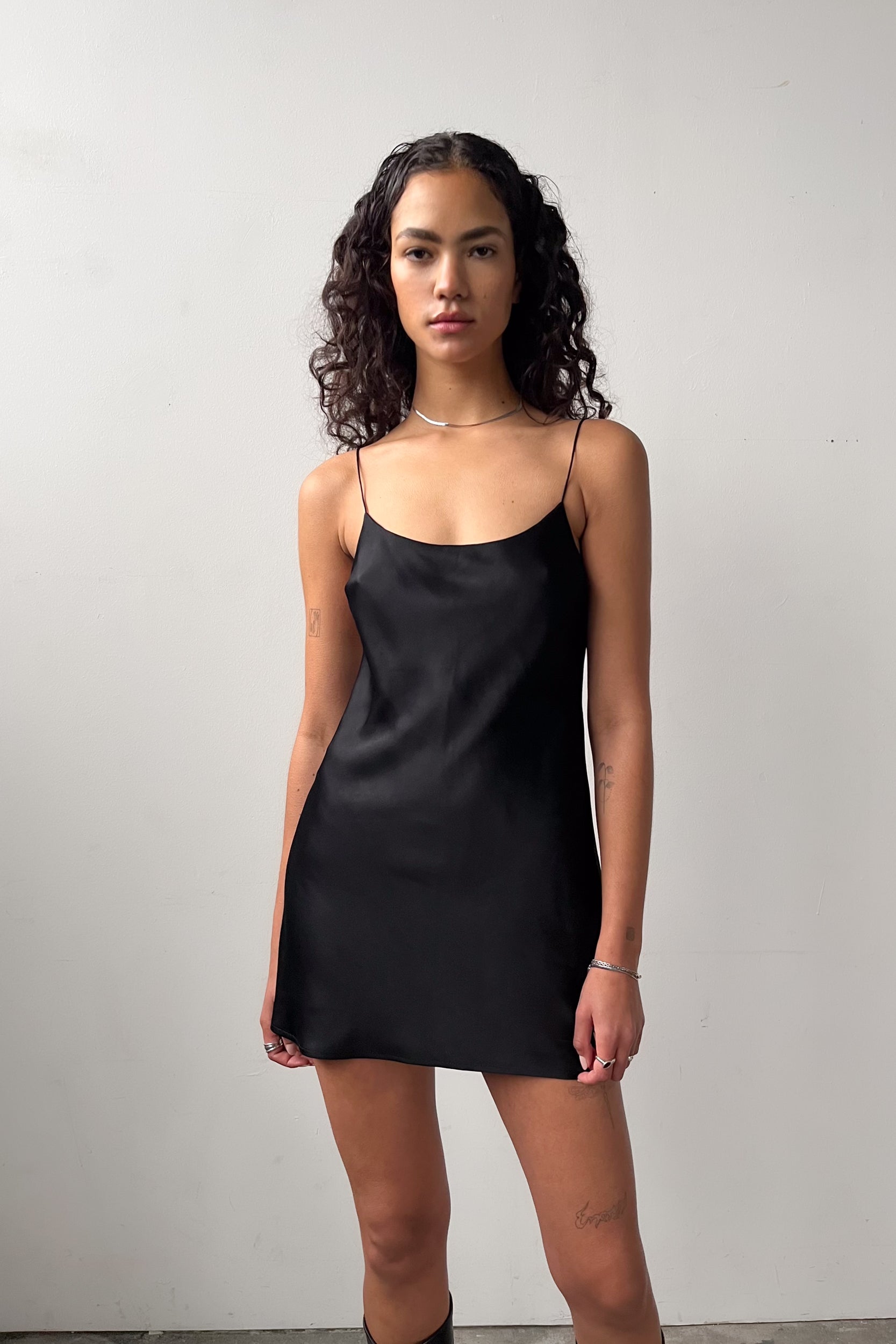 Front view of the Backless Short Slip Dress in Black, featuring thin straps and a flattering silhouette in eco-certified satin.
