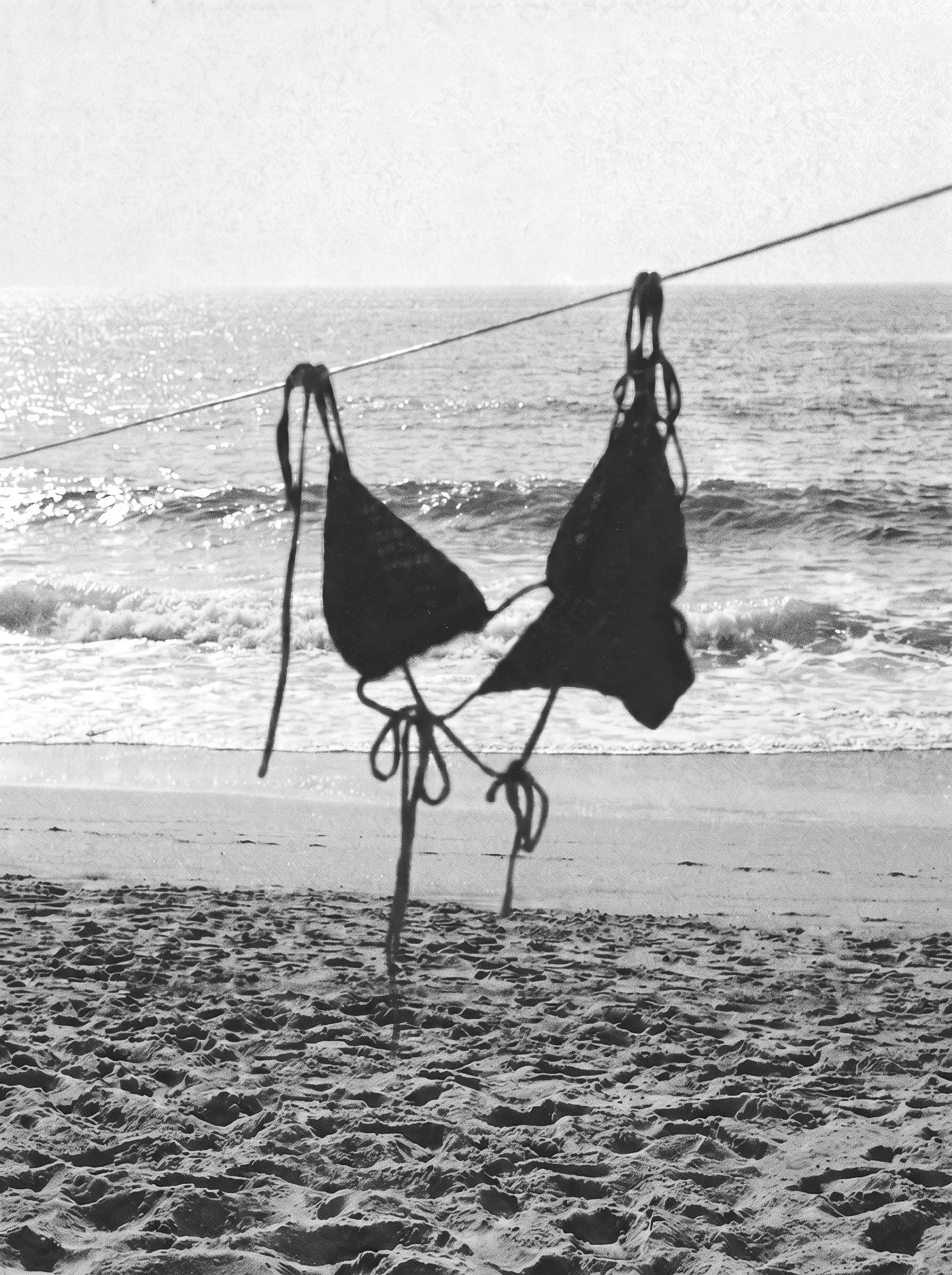 Black-and-white beach image of a model wearing the black crochet bikini top