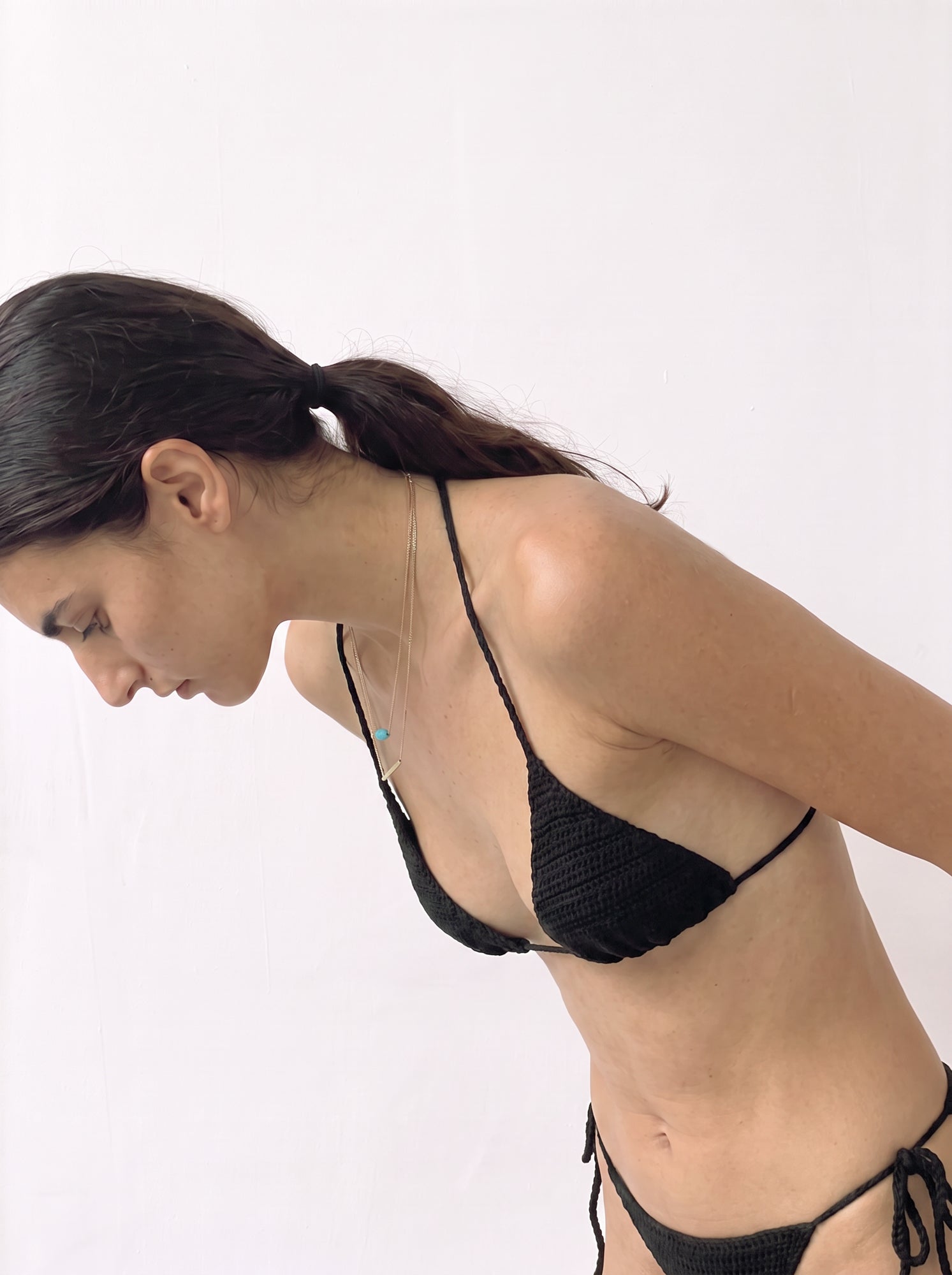 Model leaning forward in the black crochet bikini top, shown from the side