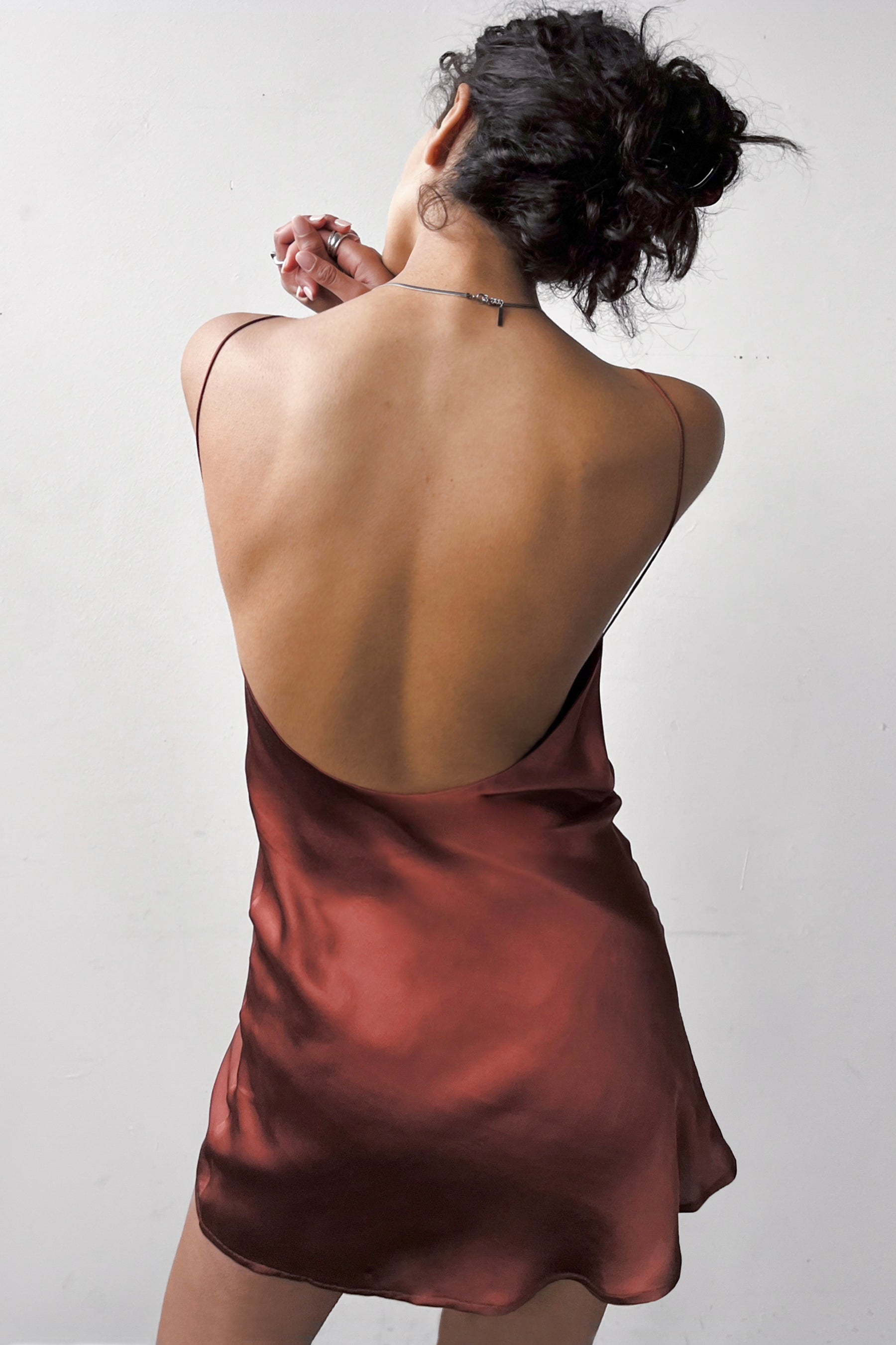 Back view of the Backless Short Slip Dress in Red, showcasing its open back design and fluid satin fabric.