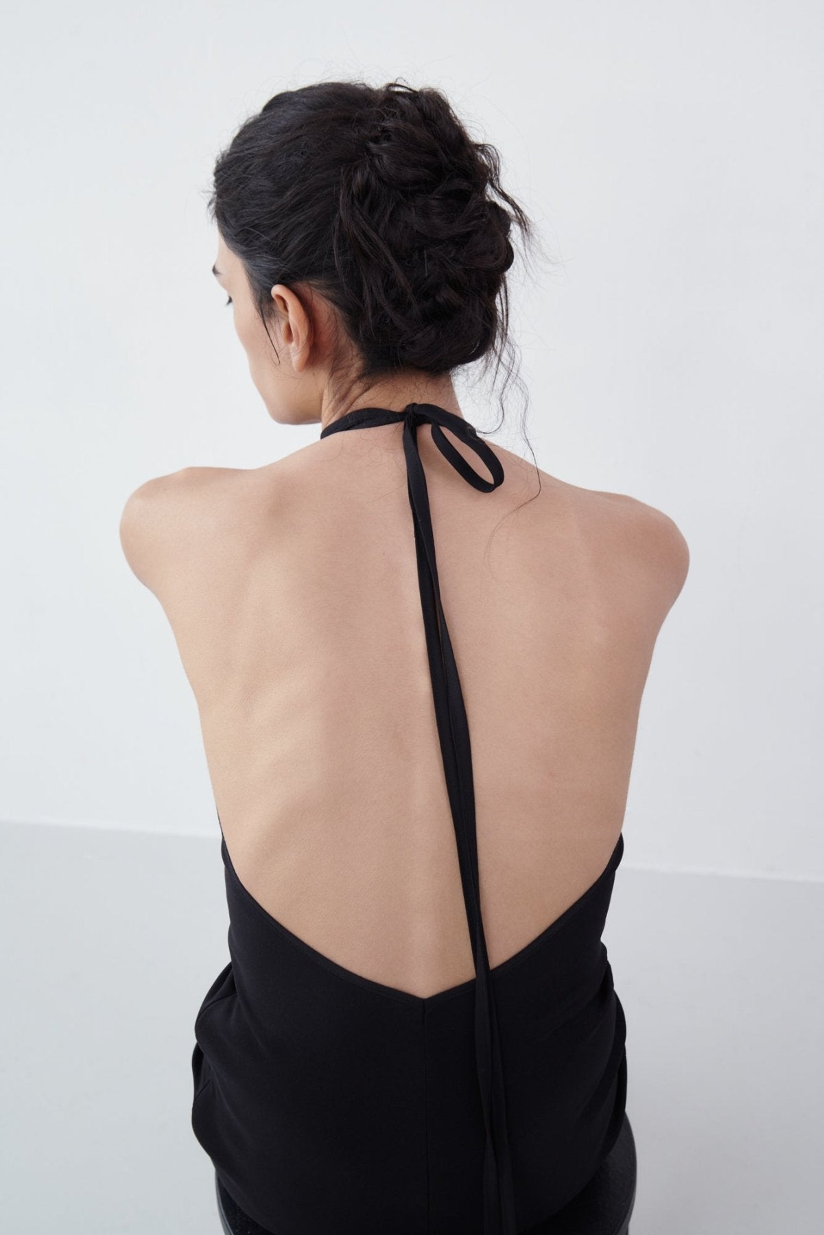 Back view of a black backless halter maxi dress showcasing the open-back design with tie detail and smooth fabric finish.