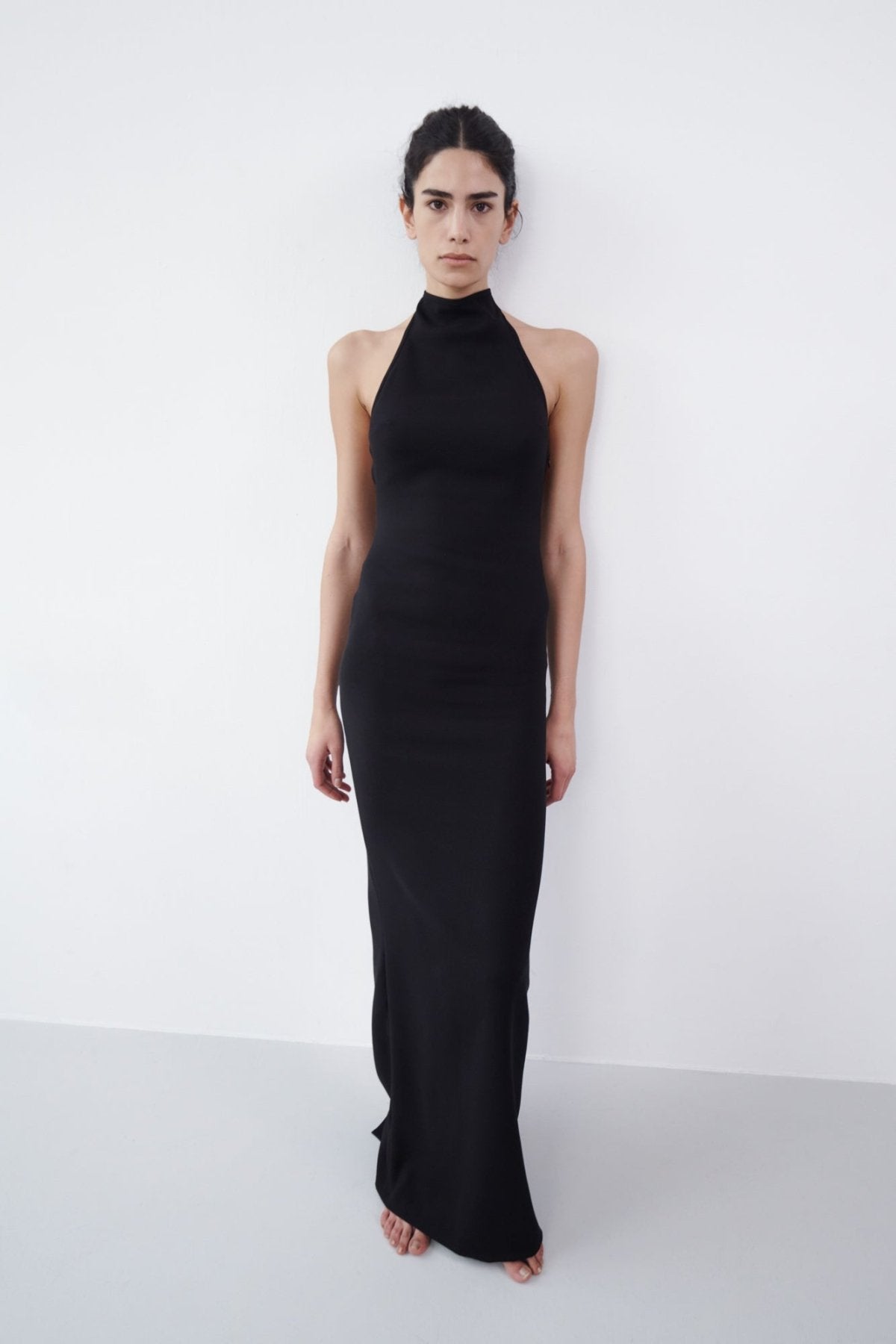 Black backless halter maxi dress with a high neckline, fitted silhouette, and maxi-length design, styled barefoot against a white background.